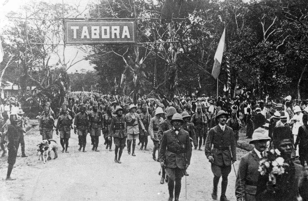 Belgian colonial troops of the Force Publique marching into Tabora under a TABORA sign, 19 September 1916