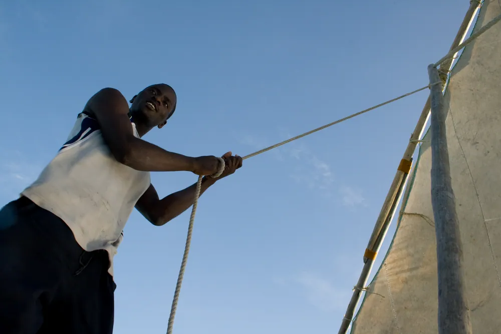 A sailor hauling on the rigging of a dhow under sail